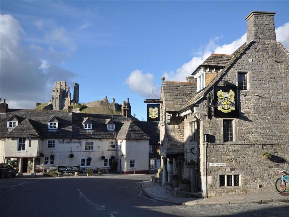A pub and stone buildings in a street with a castle in the background at Little Wickers in Wareham