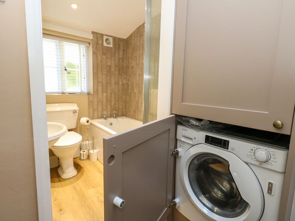 A bathroom with a toilet, bathtub, sink, and washing machine at Little Wickers in Corfe Castle