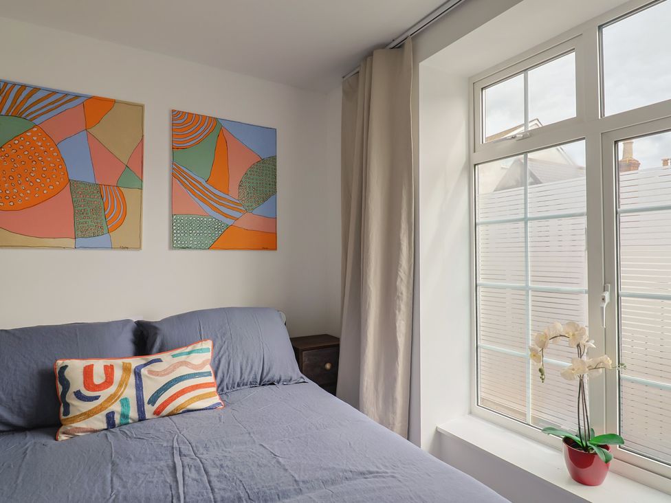 A bedroom with paintings on the wall and a window at Flat 1 Harley House Sidmouth