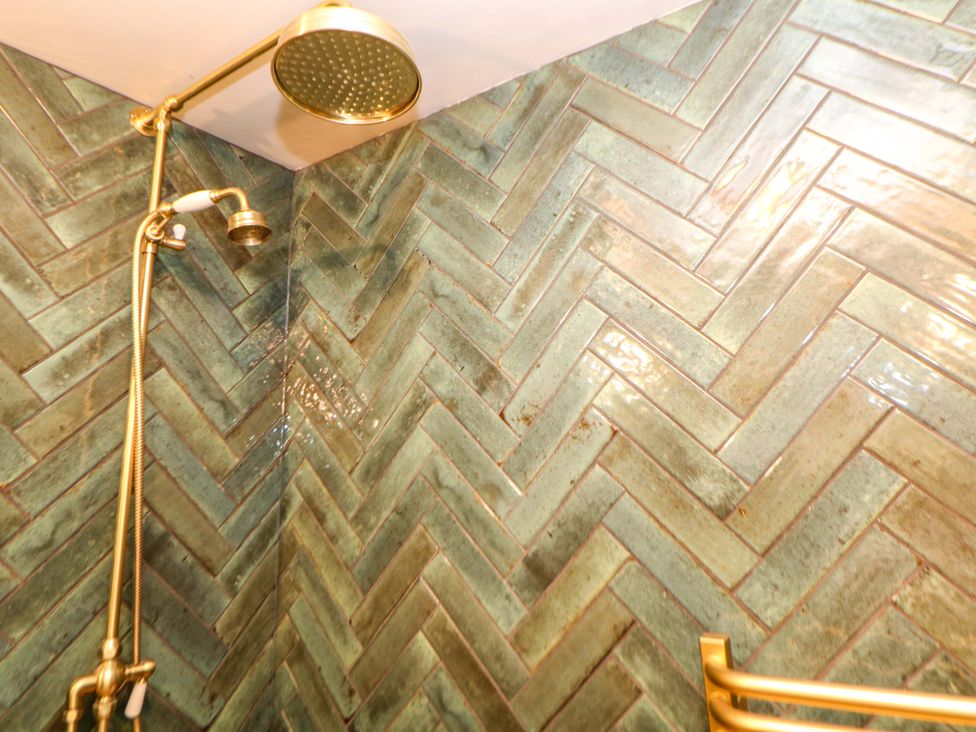 A shower head and herringbone patterned wall tiles at Bargate Cottage in Hope Valley