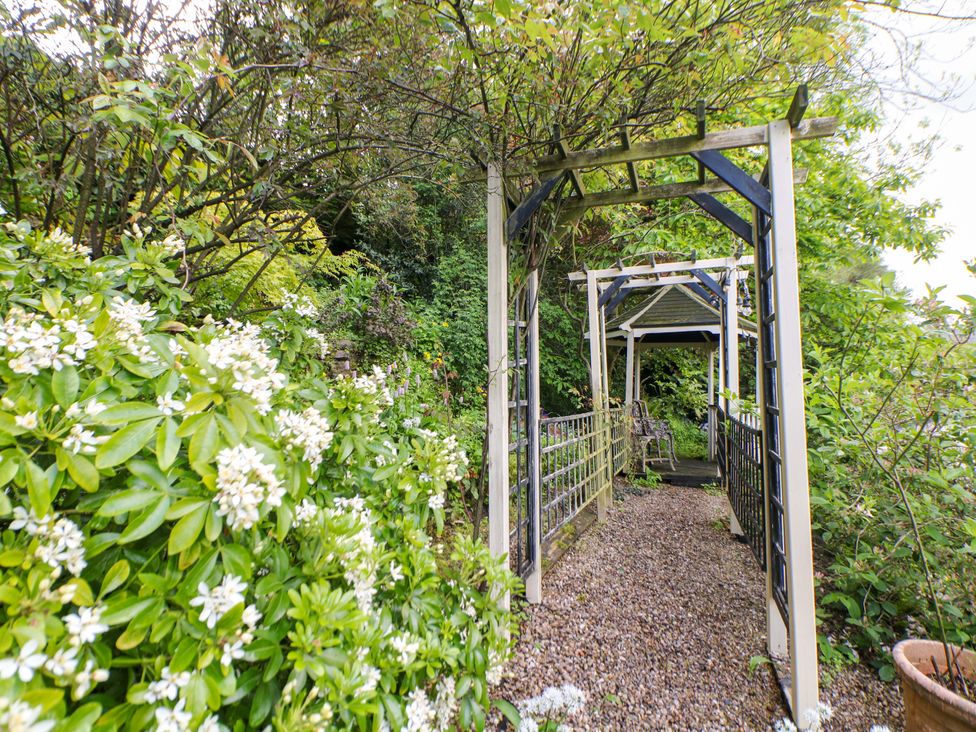 A garden pathway with flower bushes and archways at Bargate Cottage in Hope Valley