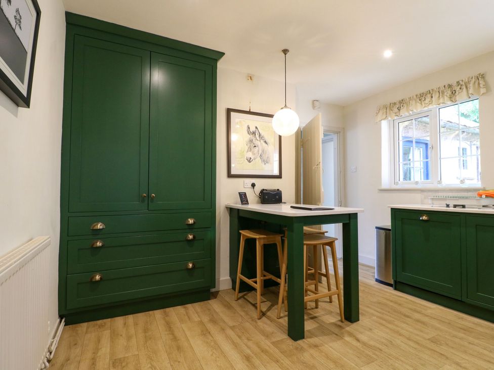 A kitchen with green cupboards and a table with stools at The Stable Flat in 