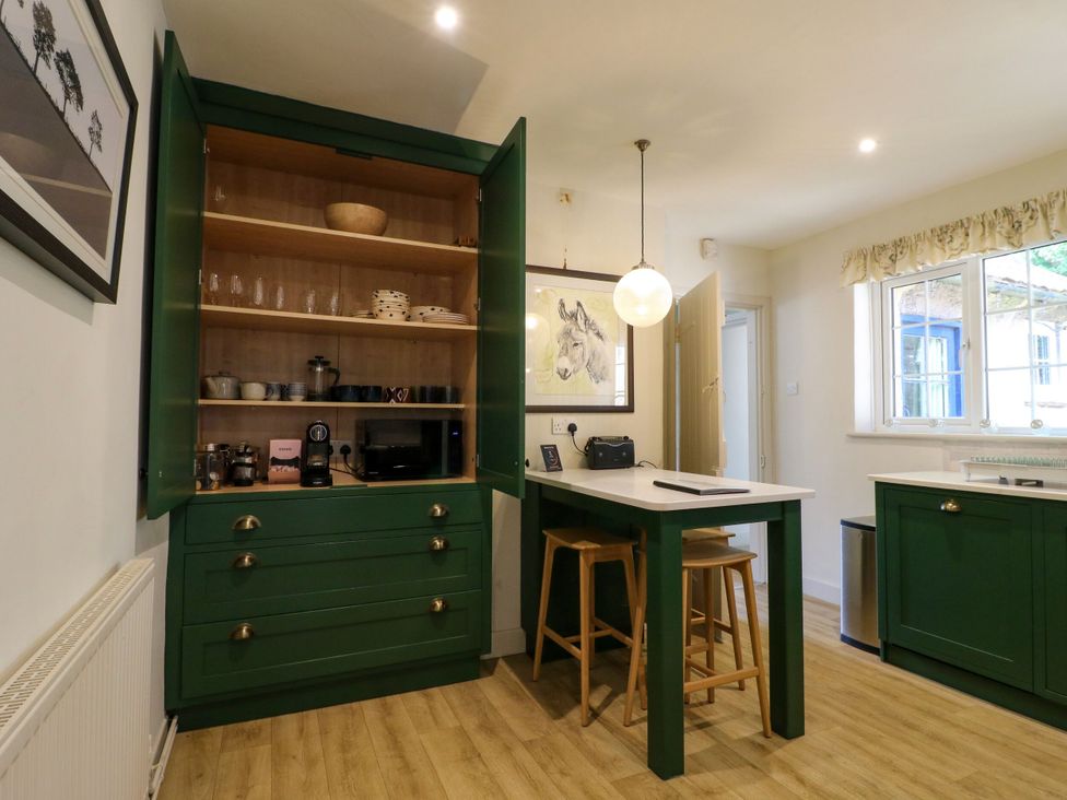 A kitchen with cupboard, microwave, and bar stools at The Stable Flat 