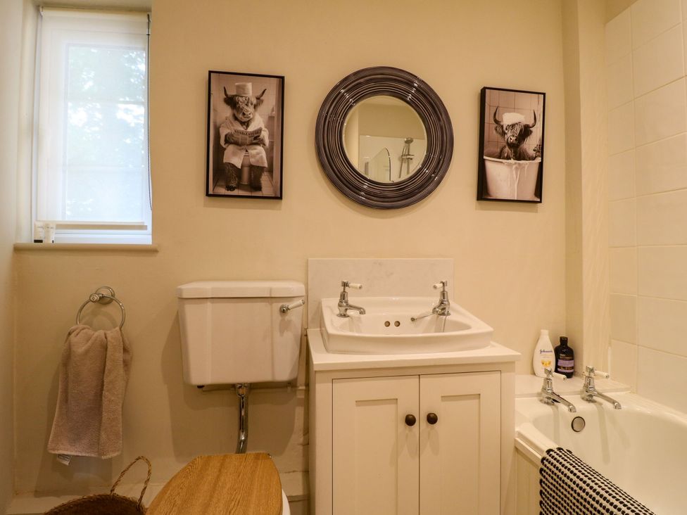 A bathroom with a sink, toilet, bathtub, and two framed artworks at The Stable Flat in 