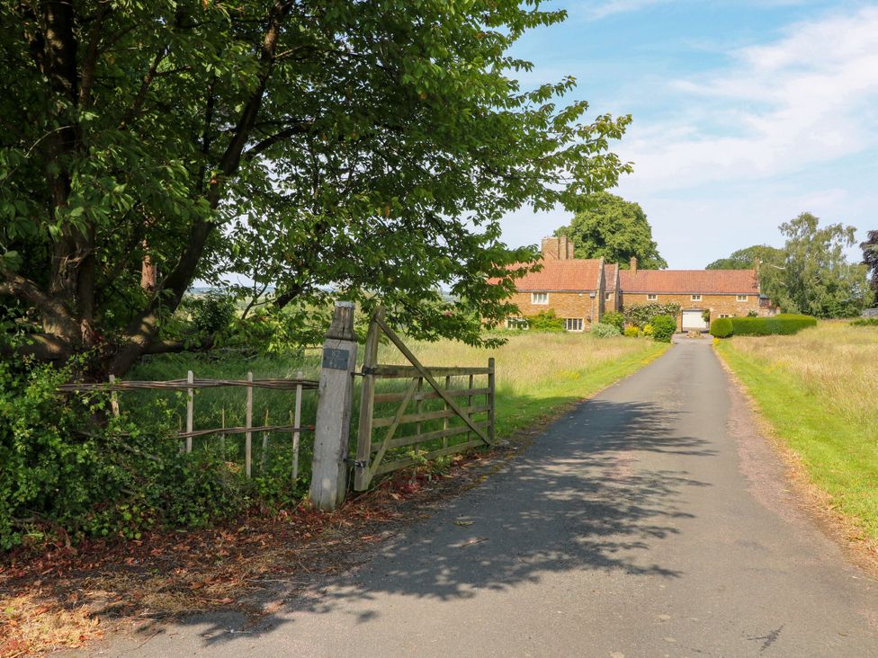 A country road leading to a building with trees and a gate at The Stable Flat