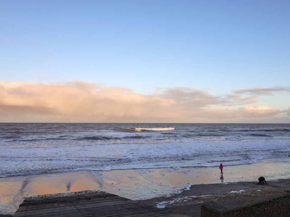 A beach with waves and a person standing at the shore at Sandy Shores Retreat in Norwich