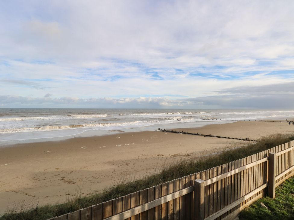 A beach with waves and a wooden fence at Sandy Shores Retreat in Norwich