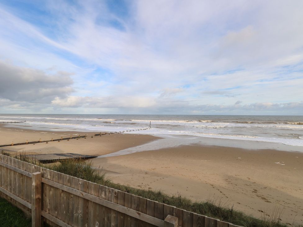 A beach with waves and a wooden fence at Sandy Shores Retreat in Norwich