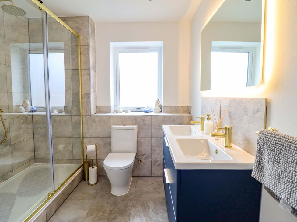 A bathroom with a toilet, shower, dual sinks and a window at Kingfisher