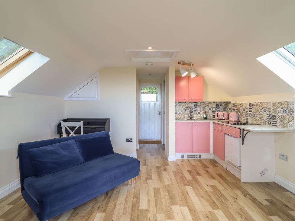 A kitchen area with a sofa and pink cabinets at Hay Loft at Ebenezer Chapel in Milwr