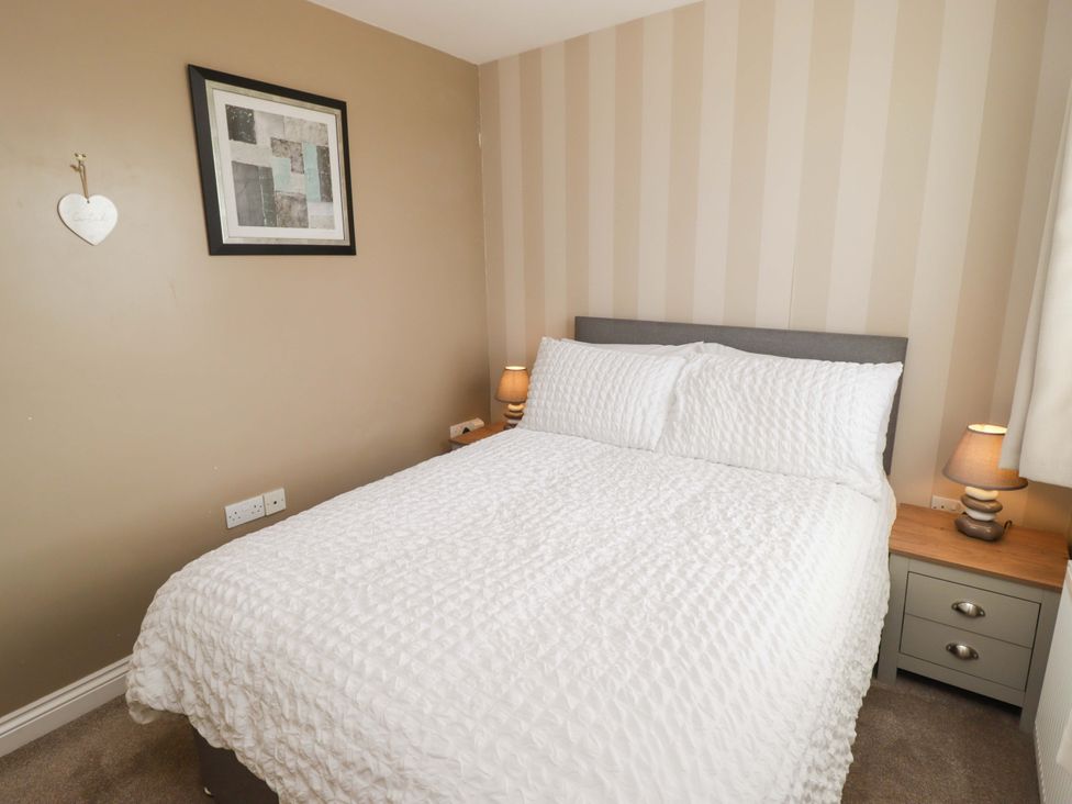 A bedroom with a bed, bedside table, lamp, and picture frame at Twyni Bach
