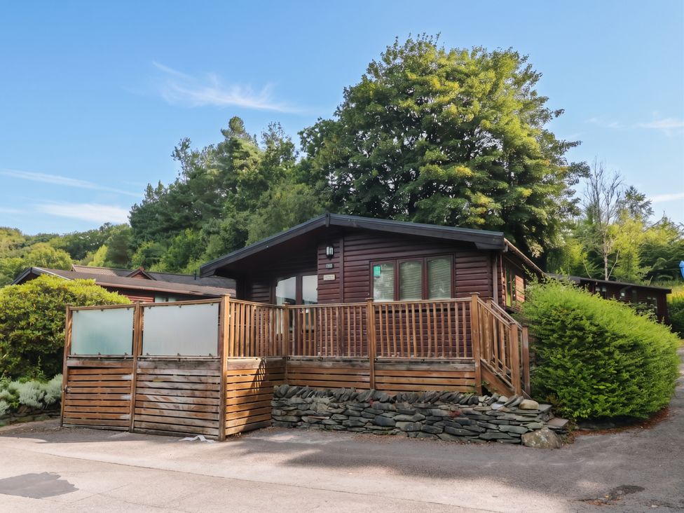 A log cabin with a wooden deck and trees at 89 Ambleside White Cross Bay