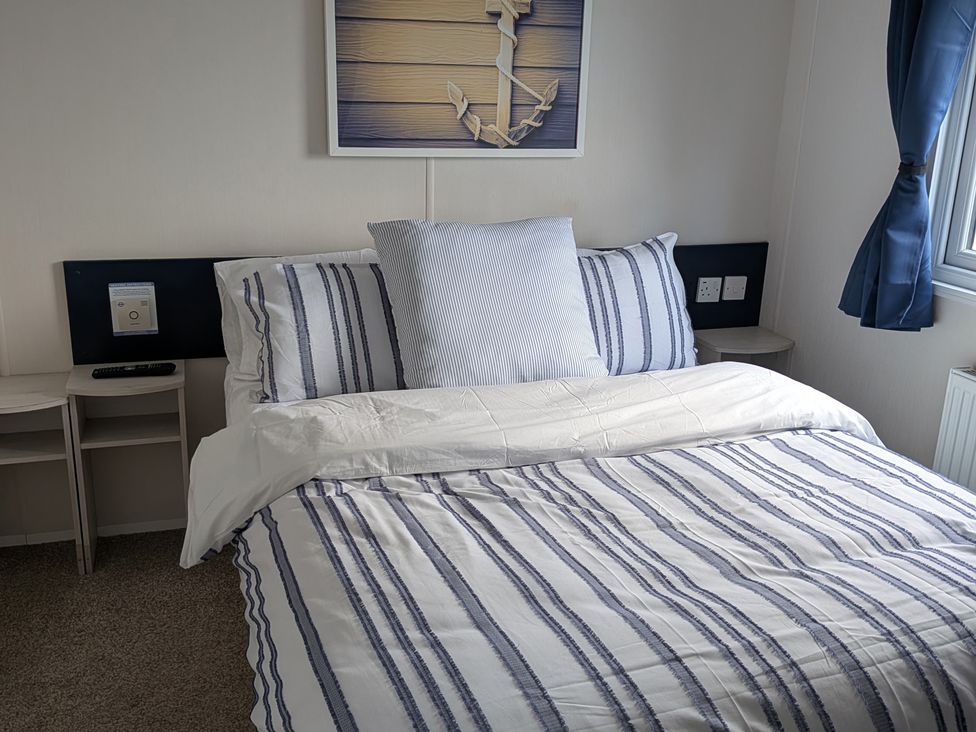 A bedroom with a bed and wall art at Presthaven - Denbigh Dunes Gronant
