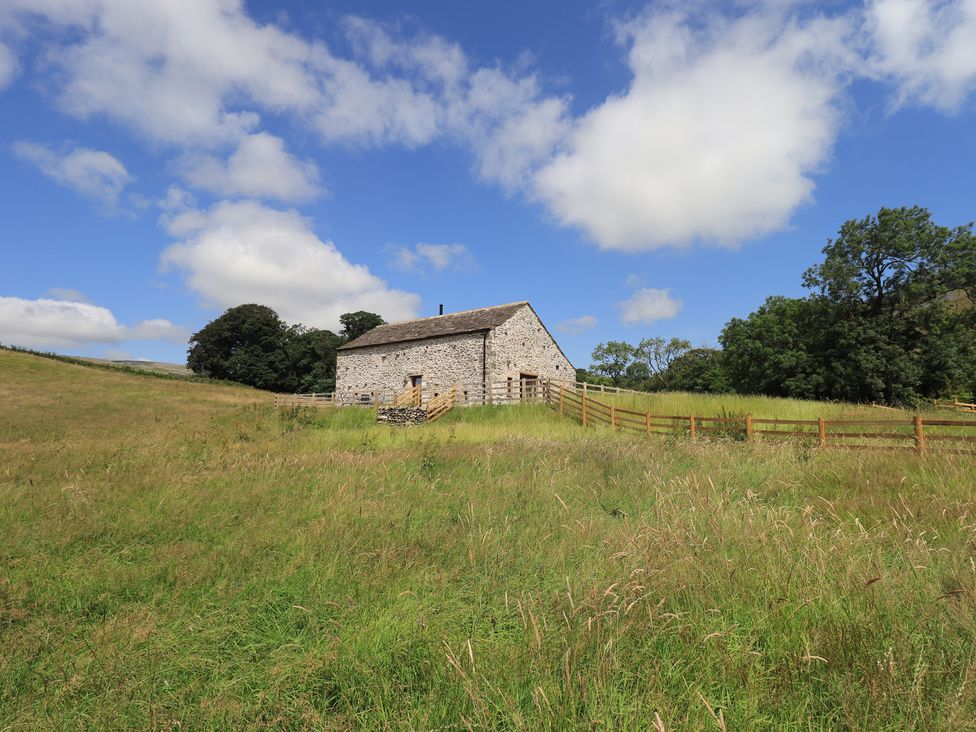 A barn with a wooden fence in a grassy field at Dam House Barn Austwick