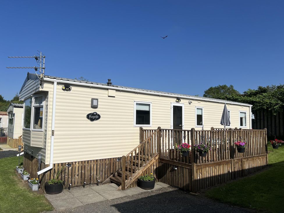 A caravan with wooden decking and potted plants at Hornshole Hideaway Caravan Hawick near Riverside Caravan Park