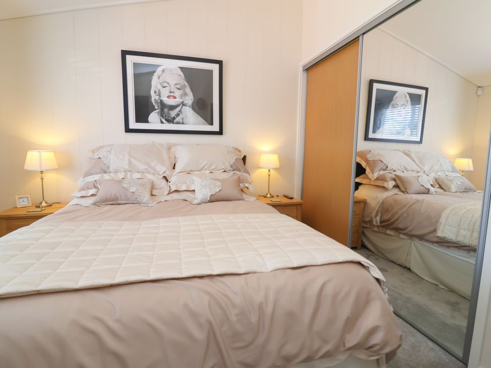 A bedroom with a bed, nightstand, and mirror at Banksy in Mullacott Park near Ilfracombe
