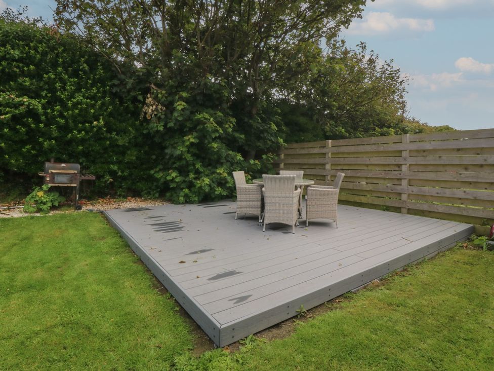 A garden with a wooden deck, table and chairs at Porth Ewyn House in Trearddur Bay