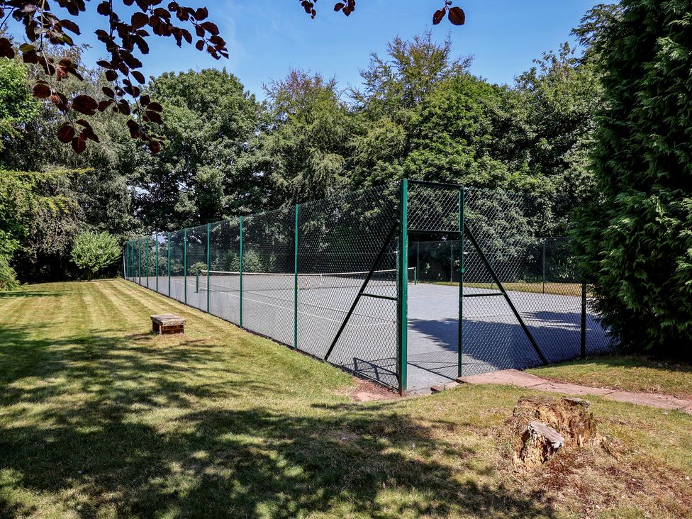 A tennis court surrounded by grass and trees at Parkfields House in Tittensor near Barlaston