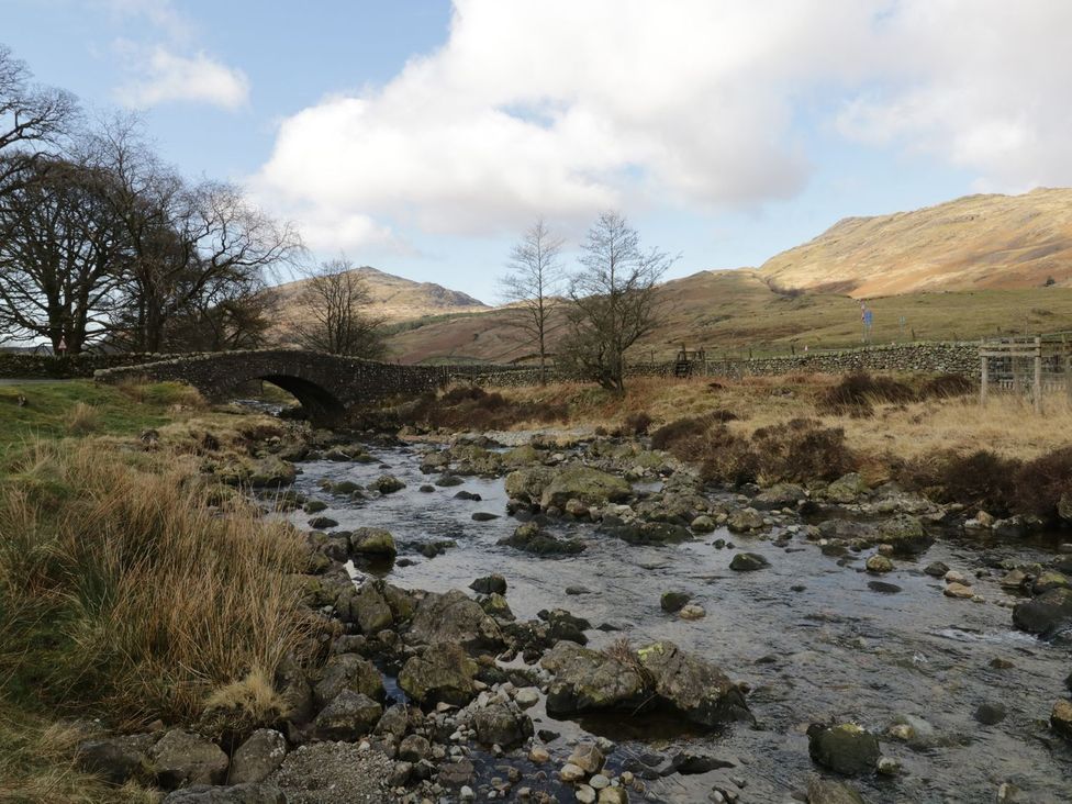 A bridge crossing a river surrounded by grass and trees at Brigg House in Broughton-in-Furness