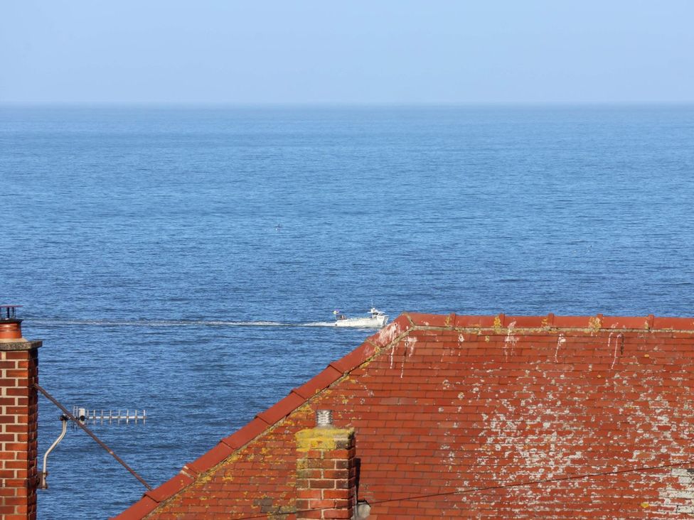 A view of the ocean with a boat and a red roof at Beachcrest in Whitby