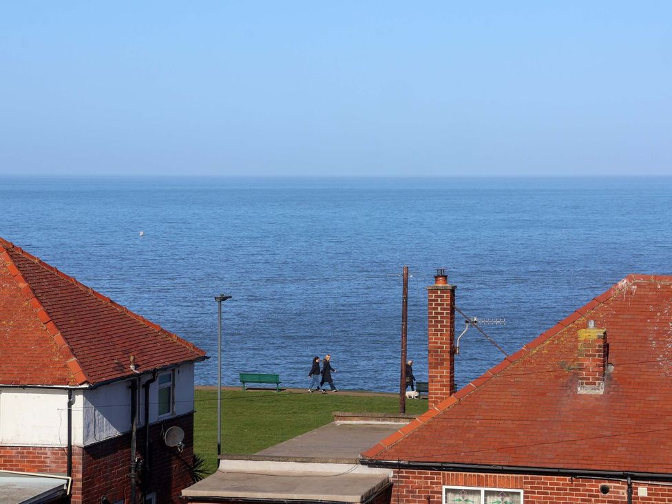 A view of the sea with a bench and people walking at Beachcrest in Whitby