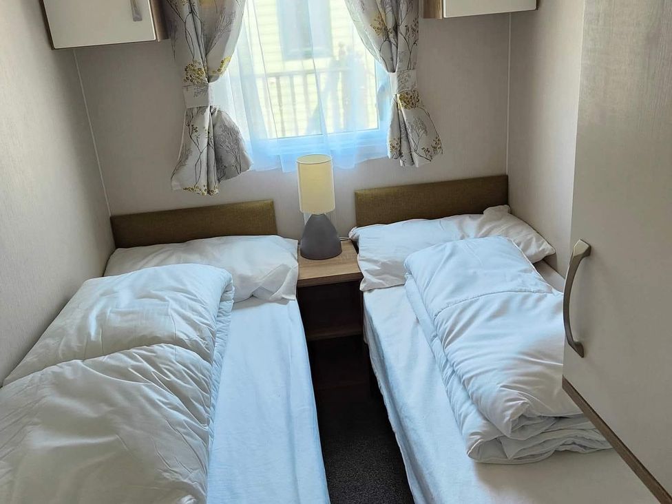 A bedroom with two beds and a lamp on a bedside table at Clarach Bay Holiday Village W18 Aberystwyth