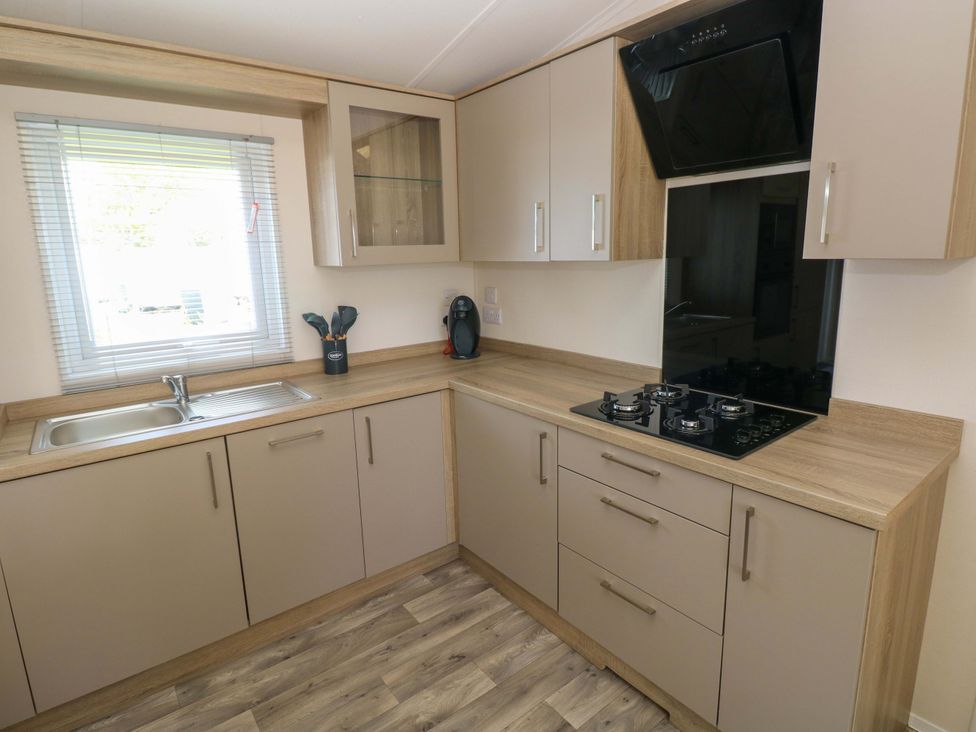A kitchen with a sink, gas stove, and cabinets at Sandpiper in Narberth