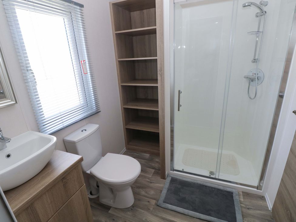 A bathroom with a sink, toilet, shower and shelves at Sandpiper in Narberth