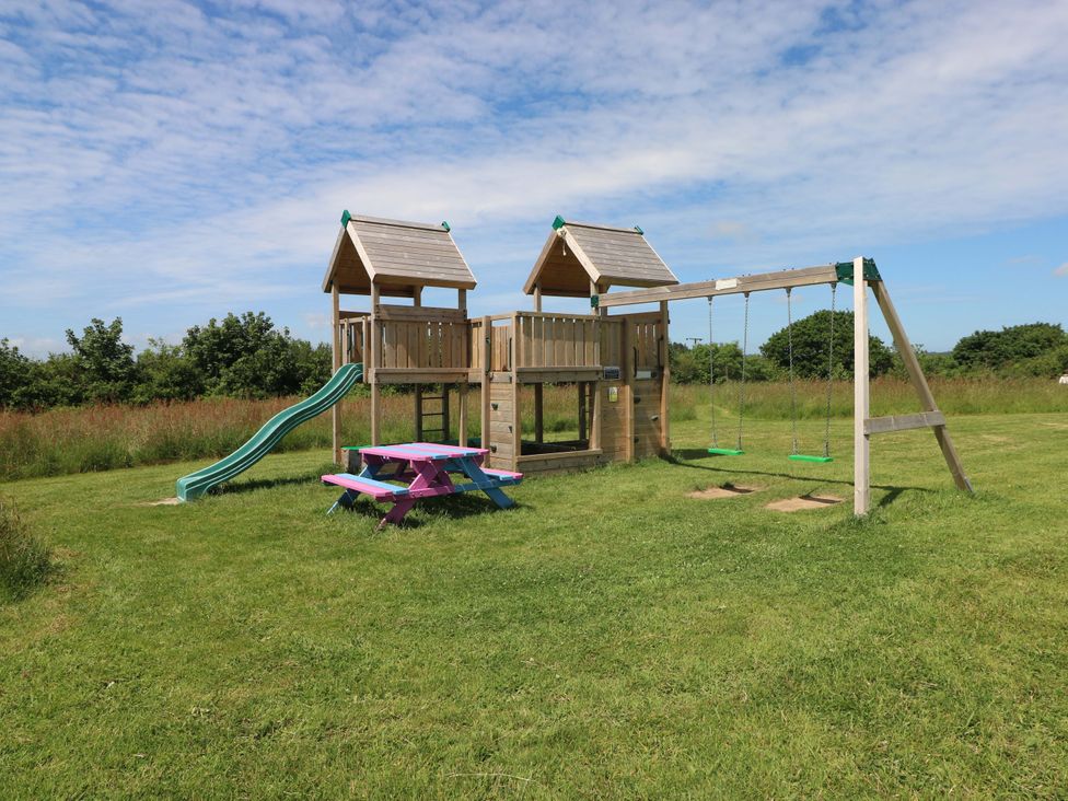 A playground with a slide and swings in an outdoor area at Sandpiper in Narberth