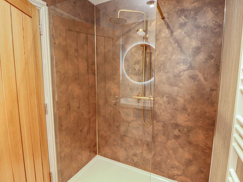 A shower with a glass panel and golden fixtures at Beckdale in Settle