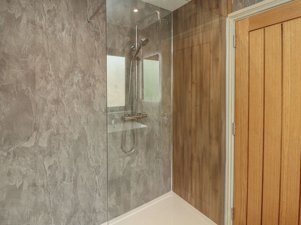 A shower area with glass wall and wooden door at Beckdale in Settle