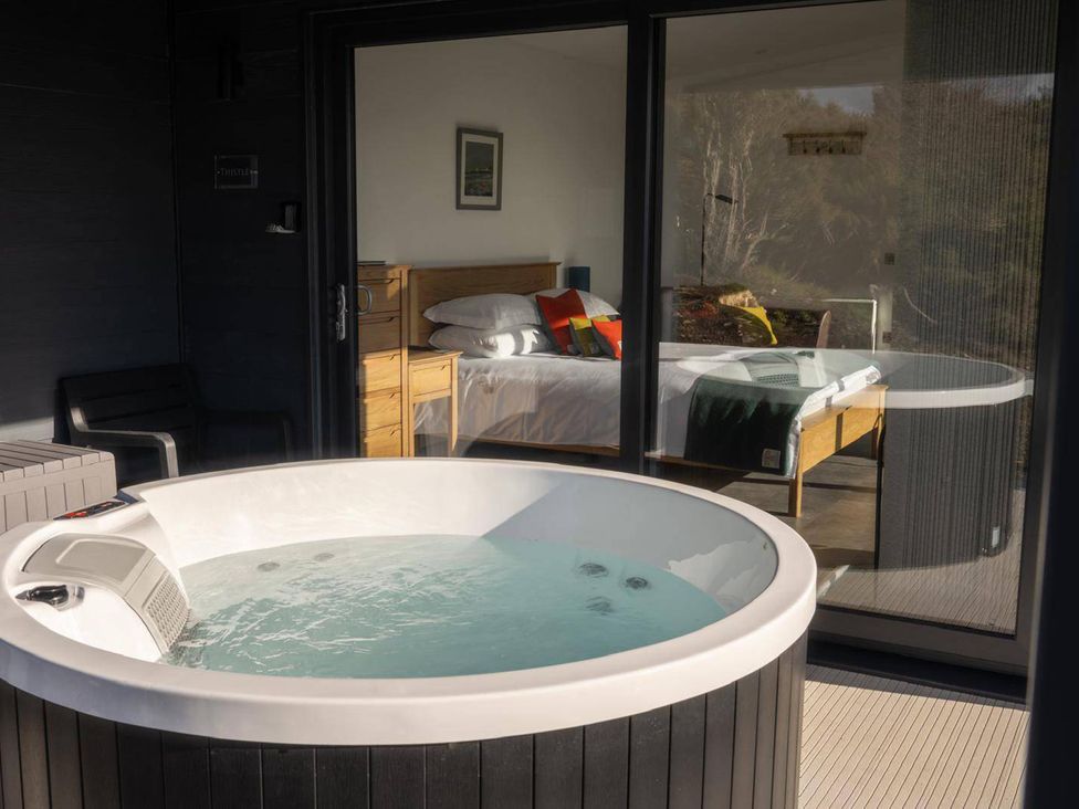 A hot tub next to a bedroom with a bed and a bedside table at Migdale Heights - Luxury Cabins in The Highlands