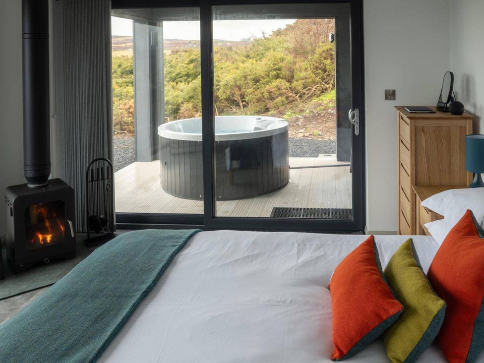 A bedroom with a bed and hot tub visible through large glass doors at Migdale Heights - Luxury Cabins in The Highlands