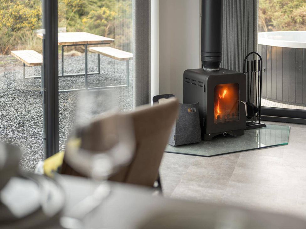 A living room with a wood stove and dining table at Migdale Heights - Luxury Cabins in The Highlands