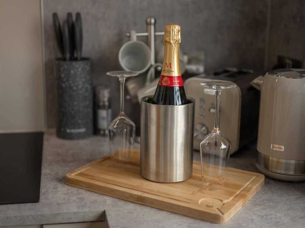 A champagne bottle in a cooler with glasses on a countertop at Migdale Heights - Luxury Cabins in The Highlands