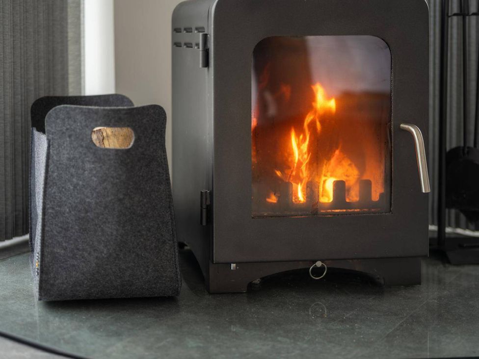 A wood stove with fire and a wood holder at Migdale Heights - Luxury Cabins in The Highlands