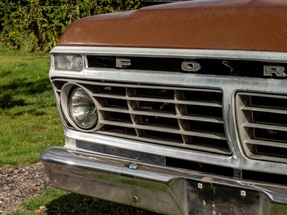 A close-up of the front grille and headlight of a Ford pickup truck in a field