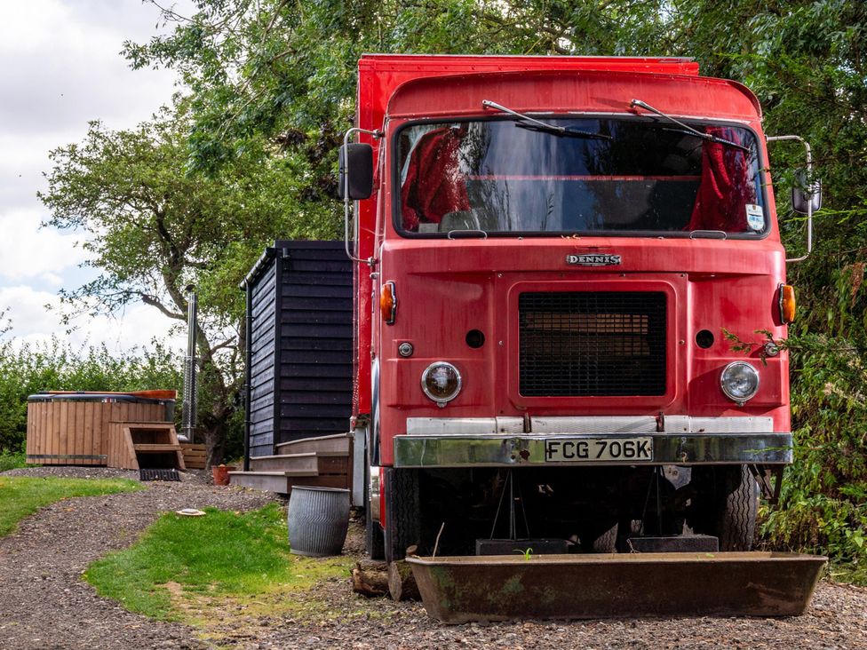 A red truck parked next to a black cabin and hot tub at Sleeps 2 -Private Garden -Pets Ok -Hot Tub -Dennis 