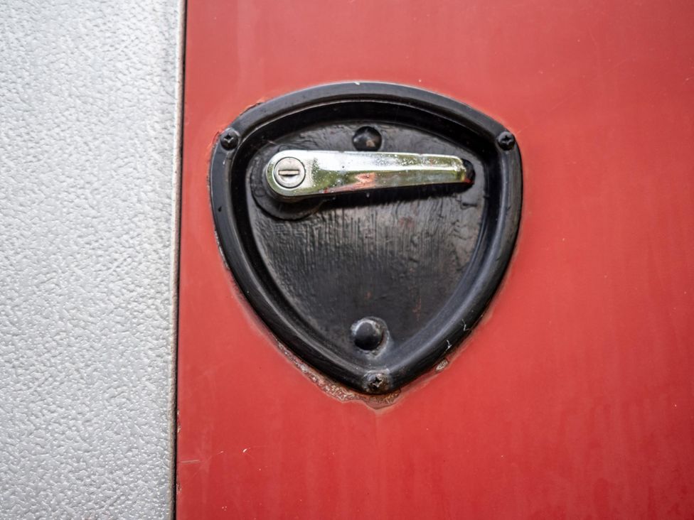 A close-up of a door lock with a handle on a red door