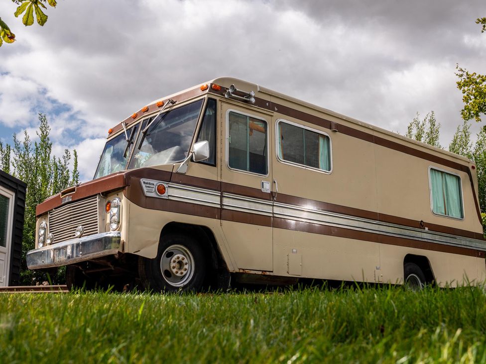 An RV parked in a grassy area with trees and clouds at Sleeps 2 -Pets Welcome -Private Hot Tub -Alabama