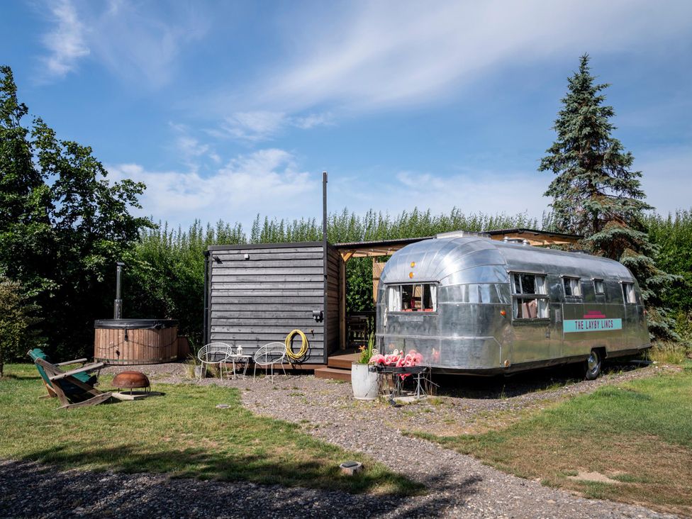 A trailer next to a wooden cabin and hot tub at The Lazy Lins in 