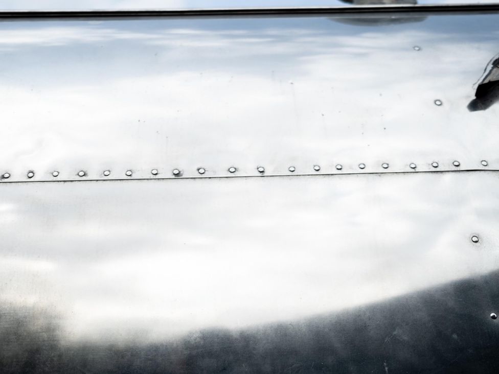 A close-up of a metal surface featuring rivets and reflections at PeggySue