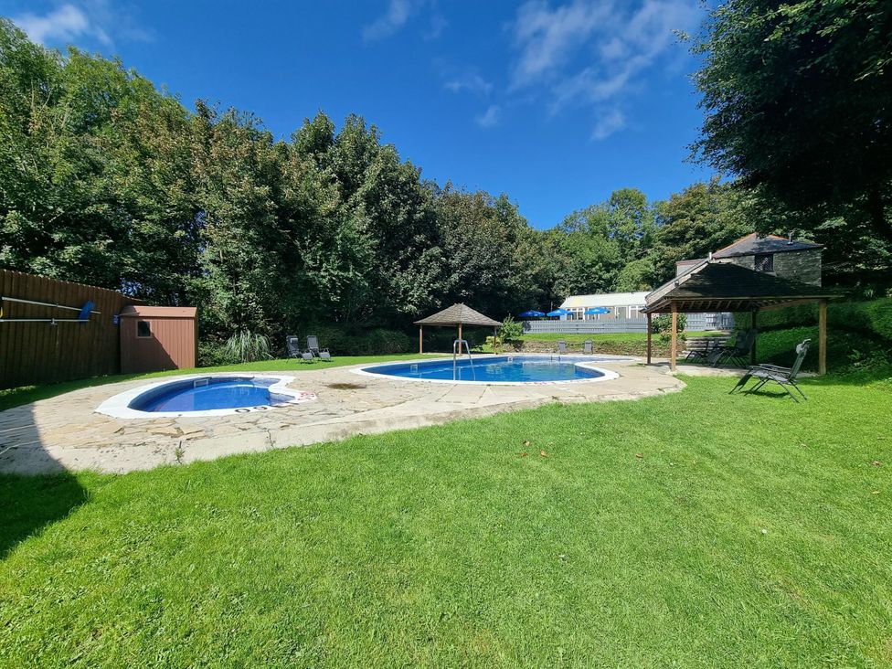 A swimming pool and hot tub surrounded by grass and trees in a garden