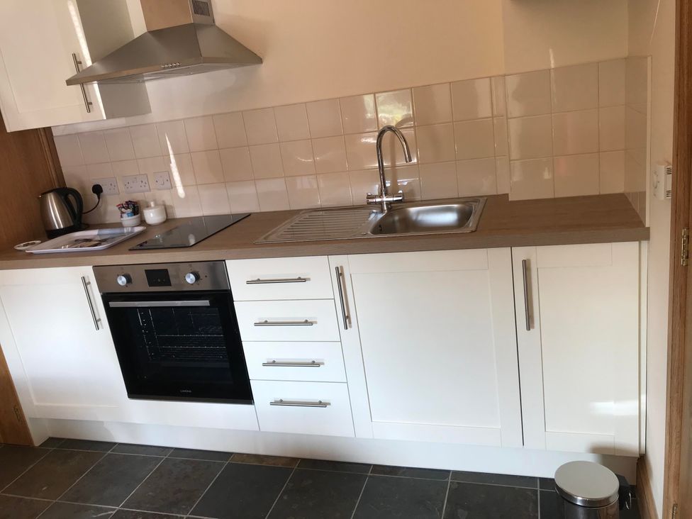 A kitchen with a sink, oven, kettle, and cupboards