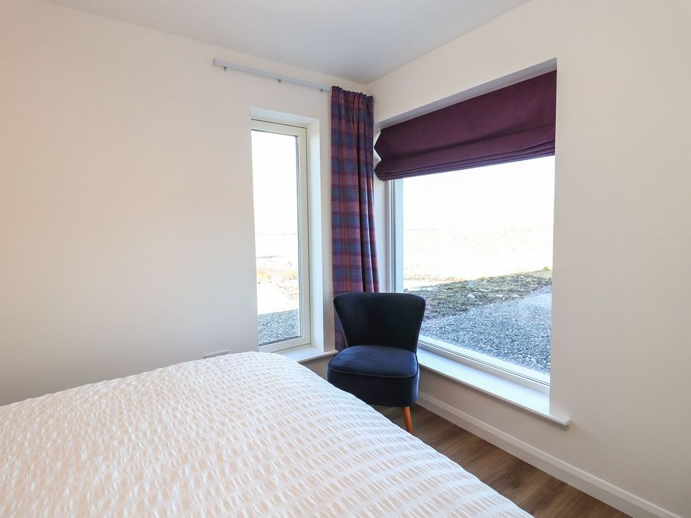A bedroom with a bed and a chair by the window at 8B Carrigreich Isle of Harris