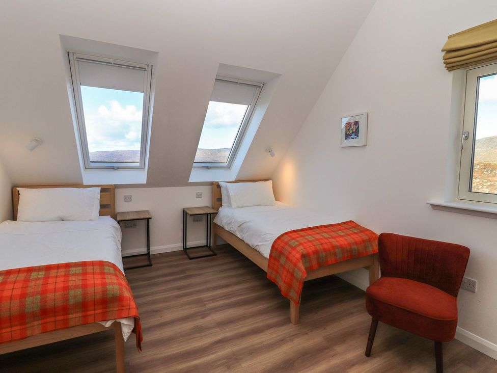 A bedroom with two beds and a chair at 8B Carrigreich Isle of Harris