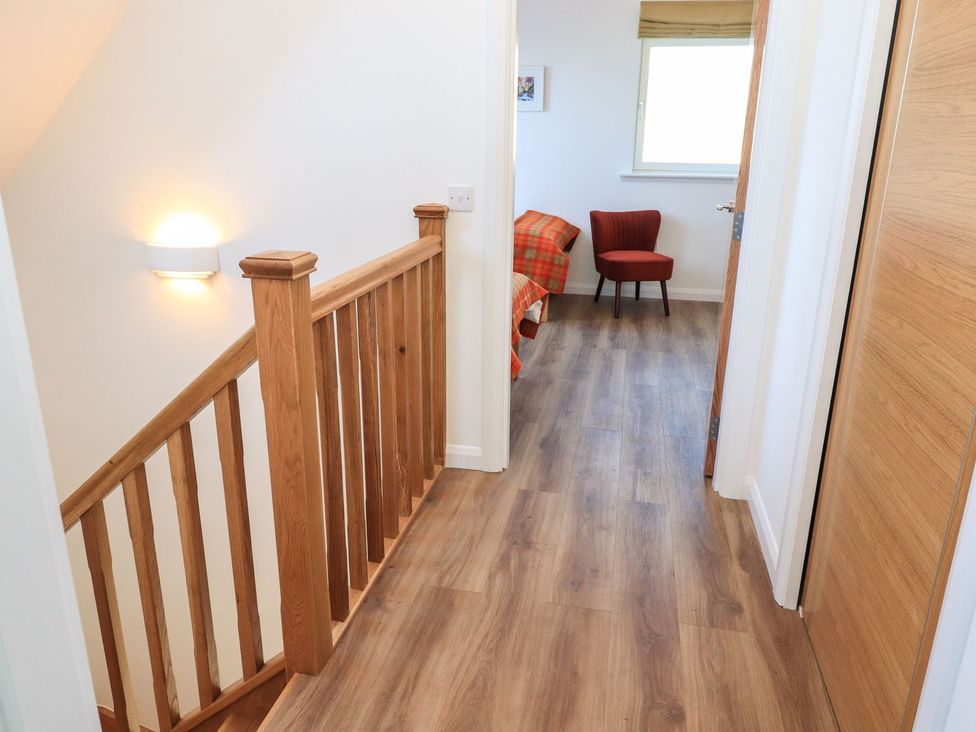 A hallway with a stair railing and a chair at 8B Carrigreich in Isle of Harris