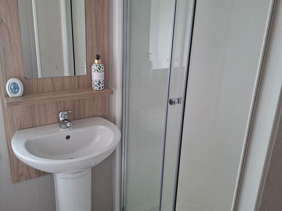 A bathroom with a sink, mirror, soap dispenser, and shower at Primrose Valley, Amara's Retreat, Filey