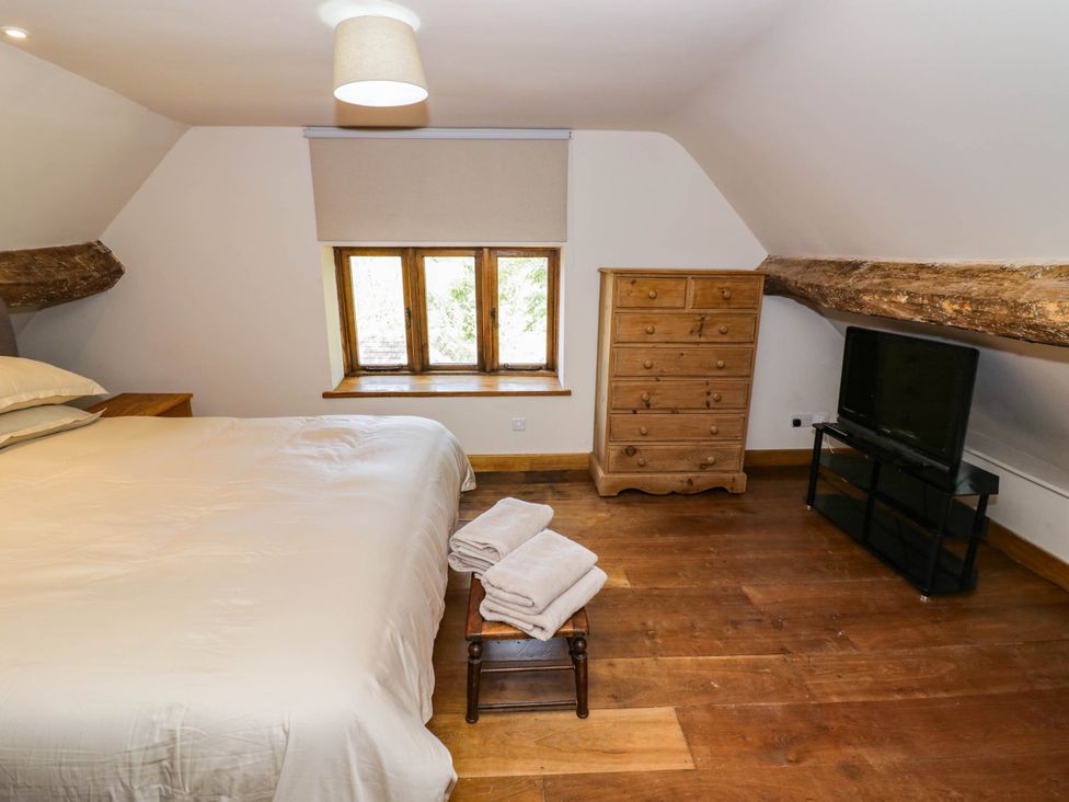 A bedroom with a bed a dresser and a television at Netherend Barn in Colwall Green near Great Malvern