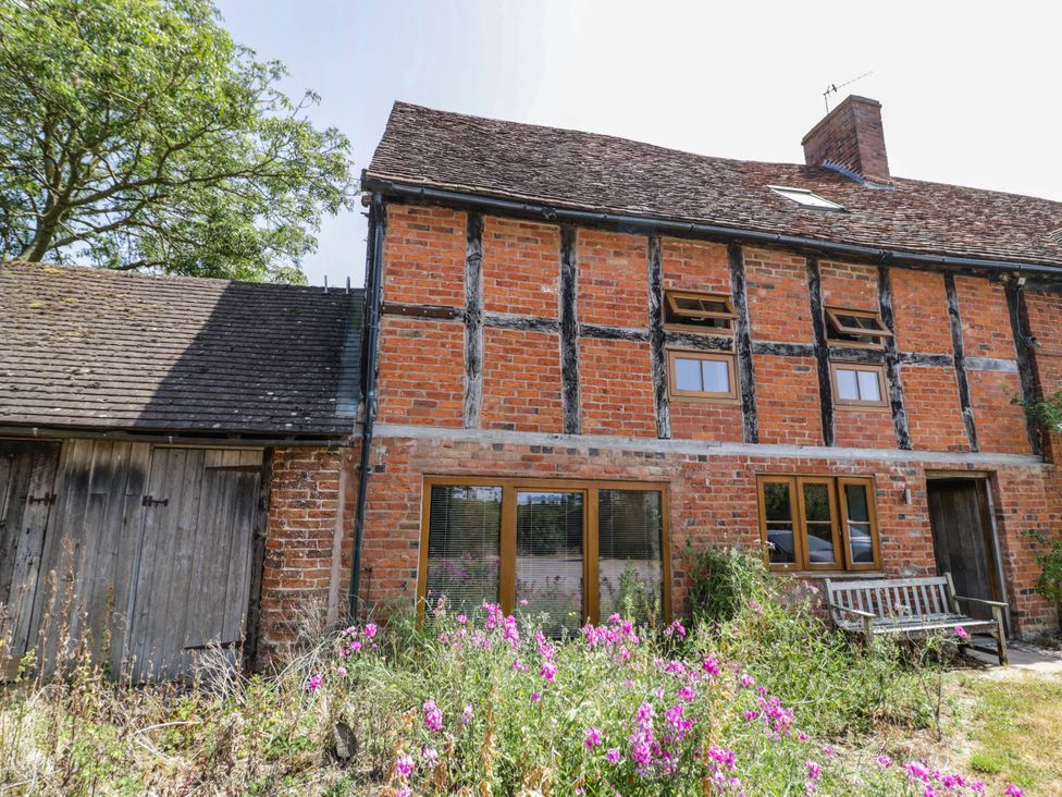 An exterior view of a brick house with a wooden bench and flowers at Netherend Barn Colwall Green near Great Malvern